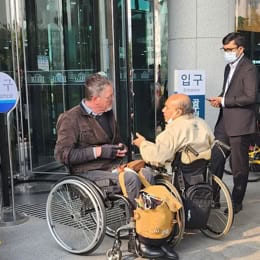 Two men using wheelchairs talking together in the entrance hall of a building.