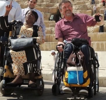 Two delegates using wheelchairs laughing together in an auditorium.