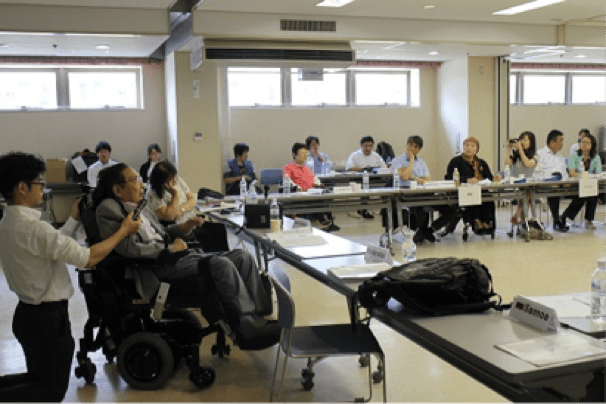Delegates, including wheelchair users, seated at tables in a meeting room.